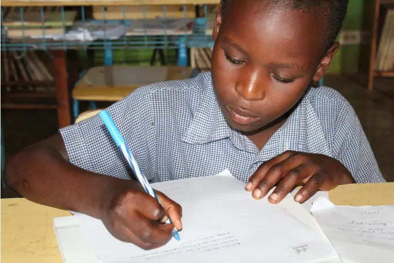 Enfant bénéficiaire des actions de PARTAGE en Haïti en classe, en train d'écrire