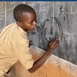 Garçon bénéficiaire du Bénin en train d'écrire sur un tableau noir