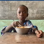 Jeune fille bénéficiaire du Bénin en train de manger un repas de la cantine scolaire en classe