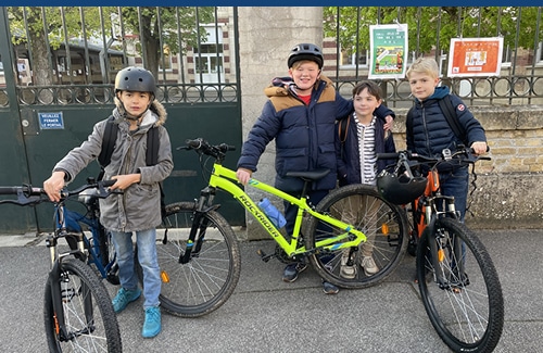 Quatre élèves en vélo devant l'école élémentaire Saint-Lazare à Compiègne dans la cadre de la journée sans voiture pour le projet « Les enfants du monde engagés pour les objectifs de développement durable » de l'association PARTAGE avec les enfants du monde